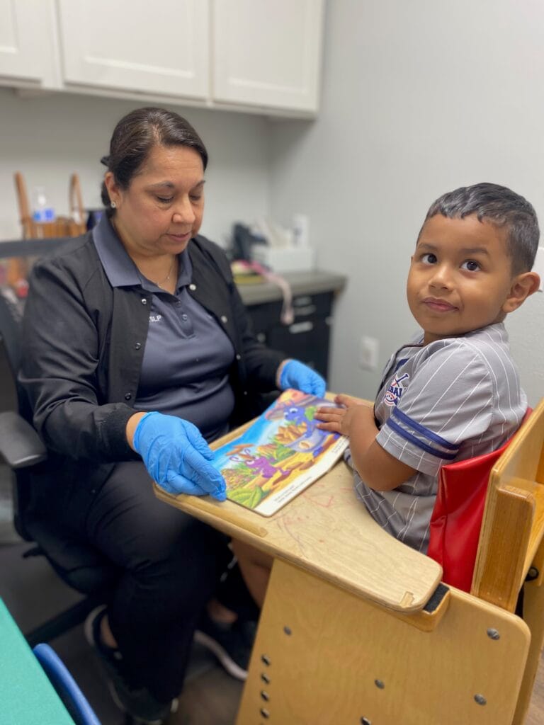 Speech therapist working with young boy on language development and communication skills using educational materials